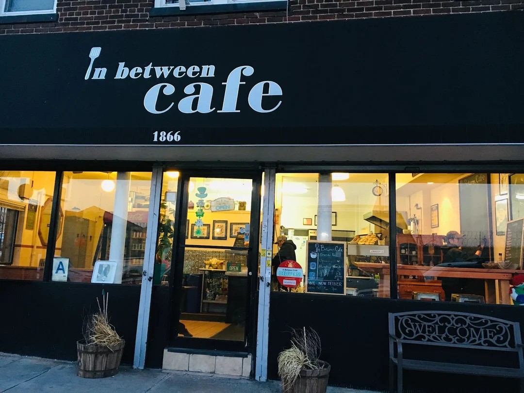 In Between Cafe storefront on Flushing Ave at dusk, warm lights glowing inside